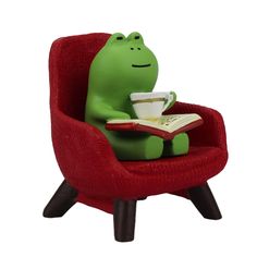 a green frog sitting in a red chair with a book and coffee cup on it's lap