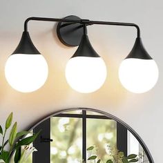 three lights on the wall above a mirror and potted plant in front of it