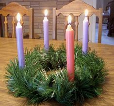 a wreath with five lit candles sitting on top of a table next to a candle holder