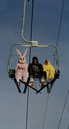 two stuffed animals sitting on top of a ski lift with people dressed as bunnies