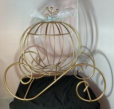 a golden metal birdcage with a bow on it's head sitting on a black cushion