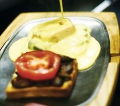 a person pouring mustard on top of a sandwich with tomatoes and cucumber slices