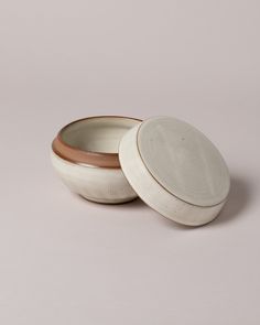 two white and brown bowls sitting on top of each other, one with a lid