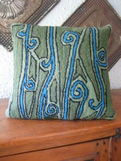 a green and blue decorative pillow sitting on top of a wooden table next to a mirror