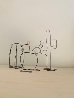 three metal cactus sculptures sitting on top of a wooden table next to a white wall