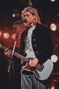 a young man playing an electric guitar in front of a microphone and some red lights