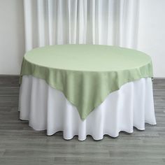 a green and white table cloth on top of a round table with curtains in the background