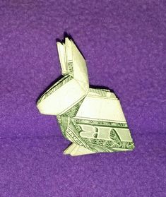 an origami rabbit made out of one dollar bill on a purple background with space for text