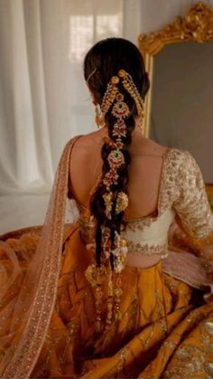 a woman with long hair wearing a yellow and gold dress sitting in front of a mirror