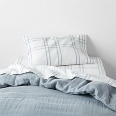 an unmade bed with blue sheets and pillows