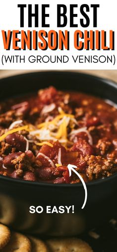 the best chili with ground venisi and cheese in a black bowl next to crackers