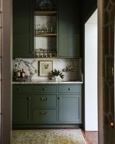 a kitchen with green cabinets and marble counter tops in the center, along with an area rug on the floor