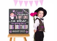 a little boy that is standing next to a sign with flowers in his hand and holding a flower