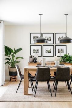 a dining room table with chairs and pictures on the wall above it, along with potted plants