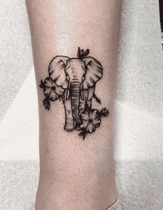 an elephant tattoo on the leg with flowers and leaves around its neck is shown in black ink