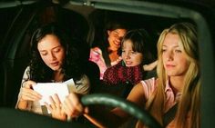 three women are sitting in the back seat of a car and one woman is holding a piece of paper