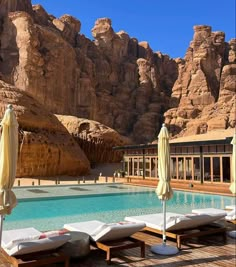 an outdoor swimming pool with chaise lounges and mountains in the backgroud