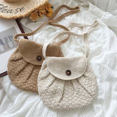 two crocheted purses sitting on top of a white bed next to a straw hat