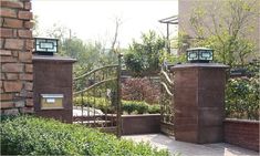 an iron gate with two lanterns on top and some bushes in the foreground behind it