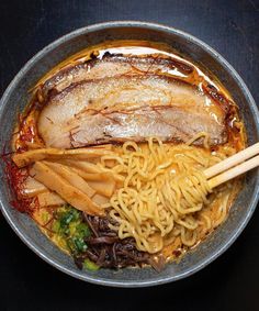 a bowl filled with noodles and meat on top of a black table next to chopsticks