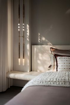 a bed sitting next to a window with white curtains and pillows on top of it