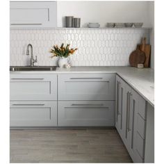 a kitchen with gray cabinets and white counter tops, an orange flower in a vase on the sink