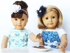 two dolls are sitting at a table with food in front of them, one is holding the other's hand