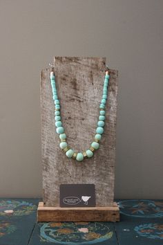 a necklace with turquoise beads is on display in front of a paper bag that has a tag attached to it