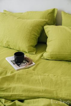 a book on a bed with green sheets and pillows in the corner, next to a black coffee cup