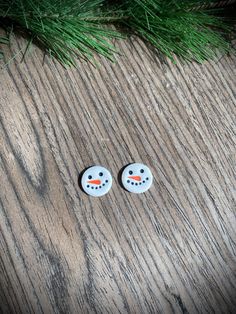 two snowman buttons sitting on top of a wooden table next to a pine tree