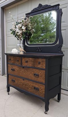 an old dresser with a mirror on top and flowers in the vase next to it