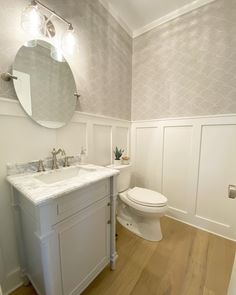 a white toilet sitting next to a sink in a bathroom under a large round mirror