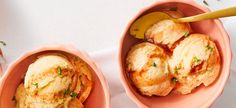 two pink bowls filled with food on top of a white table next to a yellow spoon