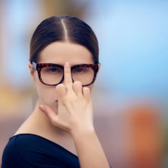 a woman wearing glasses covering her face with one hand and looking at the camera while standing in front of a blurry background