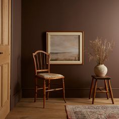 two chairs and a vase in front of a brown wall with a painting on it