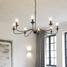 a chandelier hanging from the ceiling in a living room with windows and curtains