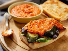 there is a sandwich on a wooden plate with sauces and bread in the background