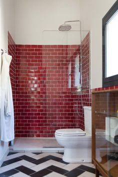 a white toilet sitting in a bathroom next to a walk in shower and red brick wall