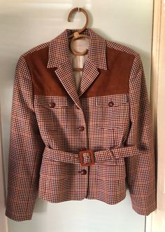 Read the full description This classic jacket is made in a beautiful rust brown combined with subtle light blue and red tartan, plaid. The shoulder part has suede brown trim at the front and the jacket itself is somewhat fitted, but with the belt you can give even more attention to the waist. The belt is detachable so you can choose. There are 2 pockets that are still stitched closed, she has beige lining that is completely intact. Just a really nice classic and also sporty jacket. She is in ver Fitted Brown Tweed Jacket For Office, Fitted Brown Sport Coat For Fall, Brown Houndstooth Tweed Jacket For Office, Brown Fall Blazer For Tailoring, Brown Houndstooth Sport Coat For Work, Brown Retro Blazer For Work, Fitted Brown Tweed Jacket Retro Style, Fall Brown Houndstooth Sport Coat, Fitted Brown Belted Outerwear