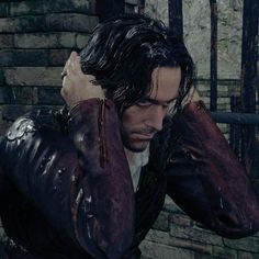 a man in a leather jacket holding his hands to his head while standing next to a brick wall