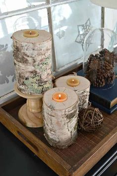 three candles sitting on top of a wooden tray next to pine cones and other decorations