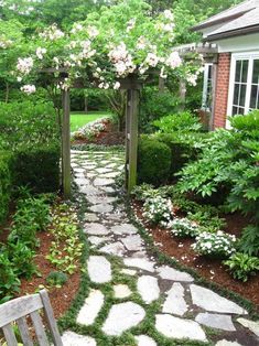 a wooden bench sitting in the middle of a garden next to a stone path with white flowers on it