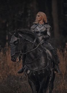 a woman dressed in armor riding on the back of a black horse through tall grass