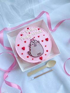 a pink birthday cake with a hippo face on it in a box next to utensils