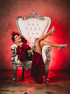 a woman sitting on top of a white chair next to a red wall and wearing high heels