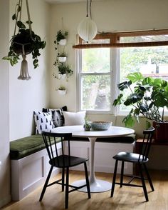 a table with two chairs and a bench in front of a window filled with potted plants