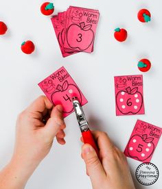 a person cutting out pink paper with scissors and apples on the table next to them