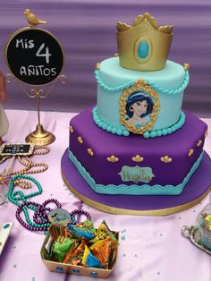 there is a purple and blue cake with a princess crown on top, surrounded by other items