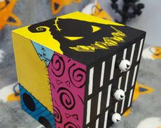 a colorful cube with black and yellow designs on the sides, sitting on a patterned surface