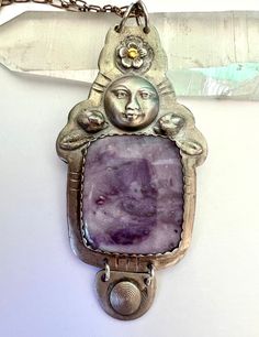 "i've used a beautiful morado opal in this piece.  also called purple opal, it doesn't have the opalescent qualities we're accustomed to, but it does have its own magic.  i've matched it with a moon face and a forget me not that has just a bit of gold leaf in the center.  the silver is 960 silver, the piece is heavy and large and hung on a sterling chain.  also some added patina. height of pendant:  3 and 5/16\" width:  1 and 11/16\" length of chain:  20\"" Mystical Amethyst Moon Phase Jewelry, Handmade Celestial Purple Jewelry, Handmade Purple Celestial Jewelry, Purple Handmade Celestial Jewelry, Celestial Amethyst Jewelry For Healing, One Of A Kind Artisan Purple Jewelry, Mystical Moon Phase Purple Jewelry, Mystical Purple Moon Phase Jewelry, Unique Purple Cabochon Jewelry